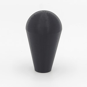 Puede incluir: Una perilla de joystick de arcade de plástico negro con una parte superior redondeada y una parte inferior cónica.