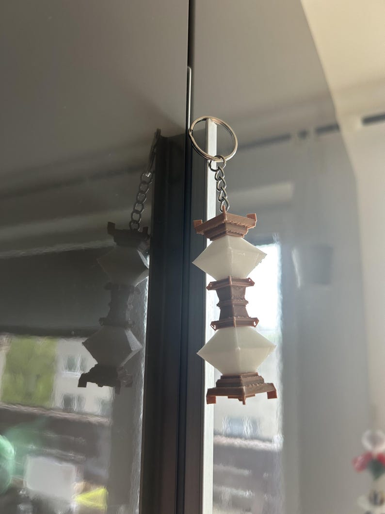 May include: A white and brown 3D printed keychain shaped like a pagoda with a silver chain.