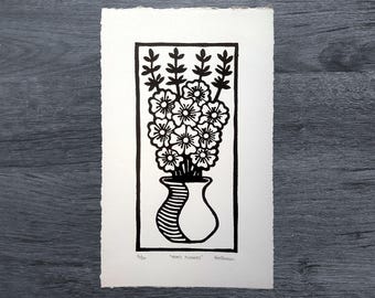 May include: Black and white linocut print of a vase of flowers. The vase is a simple, rounded shape with a striped pattern. The flowers are stylized and have a simple, geometric design. The print is titled "Mom's Flowers" and is signed by the artist.