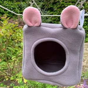 May include: A grey hanging pet bed with pink ears. The bed has a round opening for the pet to enter.