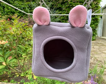 May include: A gray hanging pet bed with pink ears. The bed has a round opening for the pet to enter.