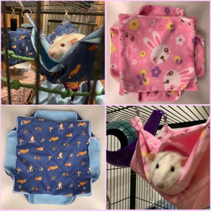 Op de afbeelding: Vier verschillende hangmatten voor ratten. De eerste hangmat is blauw met een vossenprint en een witte rat erin. De tweede hangmat is roze met een konijnenprint. De derde hangmat is blauw met een vossenprint. De vierde hangmat is roze met een witte rat erin.