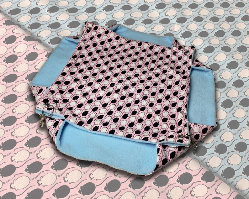 Op de afbeelding: Een blauw en roze bed met een patroon voor huisdieren met een zachte, pluche voering. Het bed is ontworpen voor kleine dieren zoals hamsters of ratten.