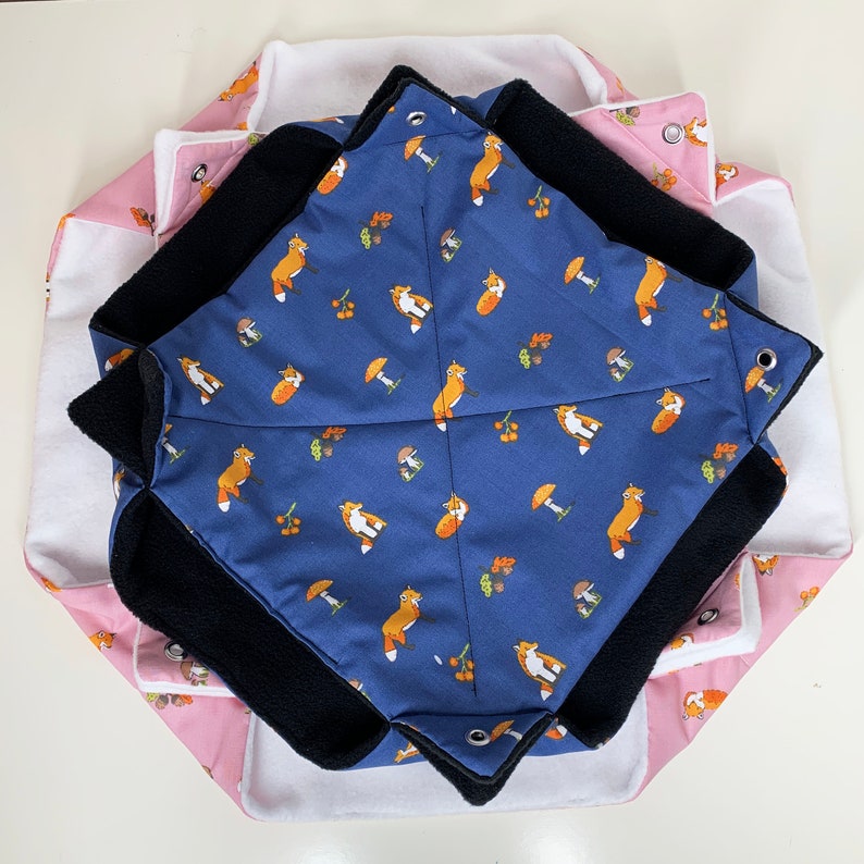 Op de afbeelding: Een blauw en zwart stoffen dierenbed met een vos-thema en een witte en roze buitenlaag. Het bed is gemaakt van zacht, comfortabel stof en heeft verschillende vos-ontwerpen.