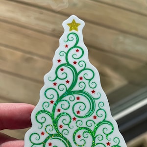 May include: A green and white Christmas tree sticker with a gold star on top. The tree is decorated with red stars and green swirls.