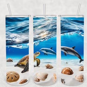 May include: A set of three stainless steel tumblers with a wraparound design featuring an underwater scene. The design includes a sea turtle, dolphins, seashells, and a sandy ocean floor with blue water and sunlight.