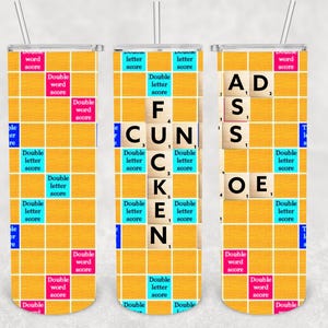 May include: Three stainless steel tumblers with a yellow Scrabble-themed design. The design features a grid pattern with letter tiles spelling out words. The tumblers have a straw and are designed for cold beverages.