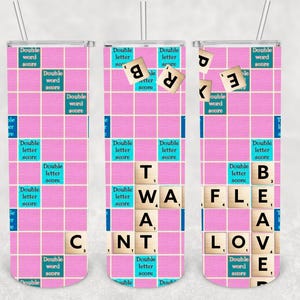 May include: Three pink and white tumbler cups with a Scrabble game design. The cups feature the words "TWAT", "FLEA", and "LOVE" spelled out in blue tiles.