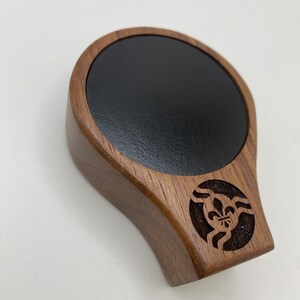 May include: A wooden coaster with a black circular insert and a carved design of a fleur-de-lis in a circle.