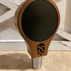 May include: A wooden beer tap handle with a black circular insert and a carved hop design.