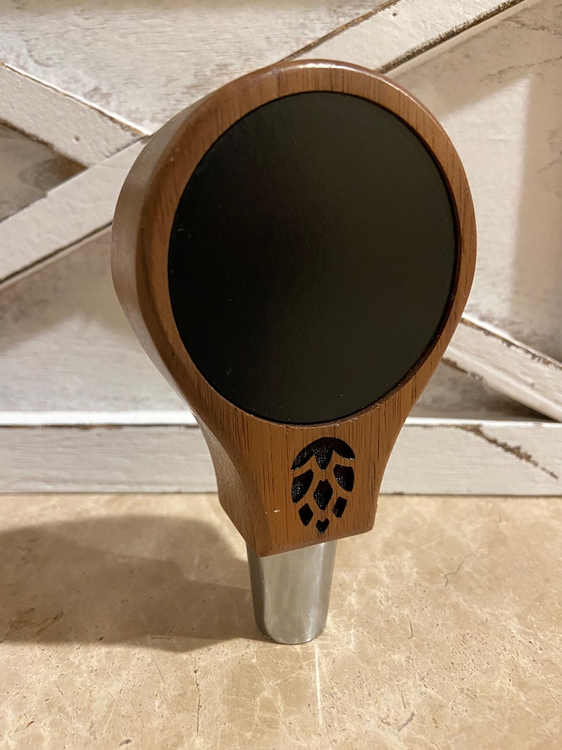 May include: A wooden beer tap handle with a black circular insert and a carved hop design.
