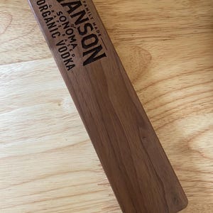 Op de afbeelding: Een houten bord met de tekst "HANSON of SONOMA GRAPE BASED ORGANIC VODKA FAMILY MADE" erop gegraveerd.
