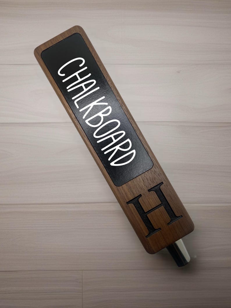 Op de afbeelding: Een houten biertap met een zwarte krijtbord-inzet met de tekst "CHALKBOARD" en een gegraveerde letter "H" aan de zijkant.