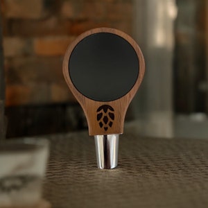 May include: A wooden beer tap handle with a black circular insert and a carved hop design.
