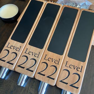 Op de afbeelding: Vier houten biertapkranen met zwarte schoolbord-inzetstukken. Elke kraan is gegraveerd met de tekst "Level 222".
