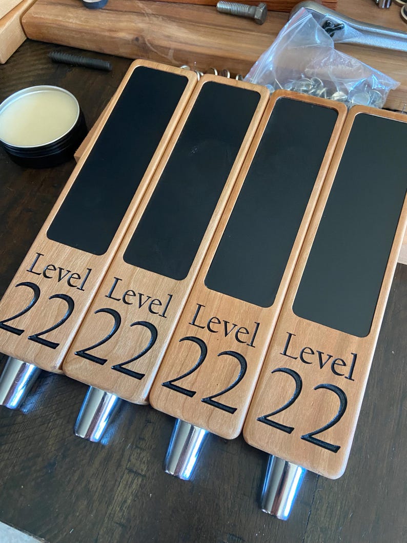 Op de afbeelding: Vier houten biertapkranen met zwarte schoolbord-inzetstukken. Elke kraan is gegraveerd met de tekst "Level 222".