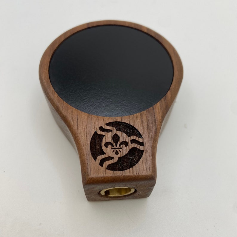 May include: A wooden beer tap handle with a black circular insert and a carved design of a fleur-de-lis and waves.