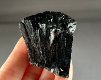 May include: A black, naturally formed, rough, and jagged crystal cluster of black tourmaline.