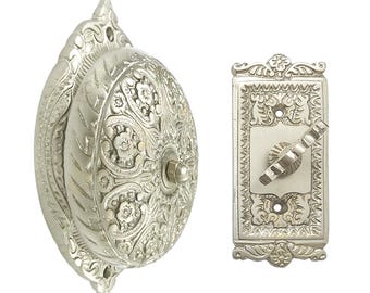 May include: A silver doorbell with an ornate design. The doorbell has a round button and a rectangular push button.