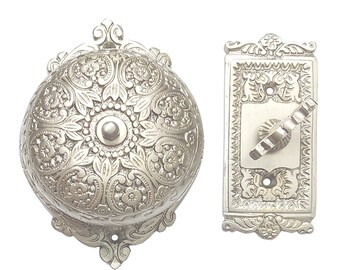 May include: Silver-colored doorbell and switch plate set. The bell is round with a floral pattern and a central button. The switch plate is rectangular with a lever and matching floral design. Decorative hardware.