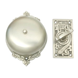 Könnte beinhalten: Eine silberne Türklingel mit einem dekorativen Design und einem Druckknopf. Die Türklingel hat ein Schild mit der Aufschrift "Turn".