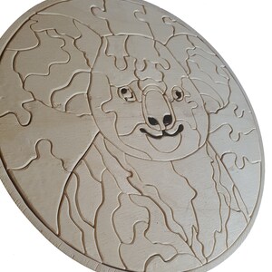 May include: A wooden jigsaw puzzle of a koala bear, with a light brown finish. The puzzle is in the shape of a circle and has a detailed design.