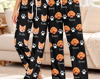 May include: Two pairs of black pajama pants featuring an all-over print of pet faces and paw prints. The left pair displays orange cat faces with the name Bella, while the right pair features brown dog faces with the name Daisy printed below.
