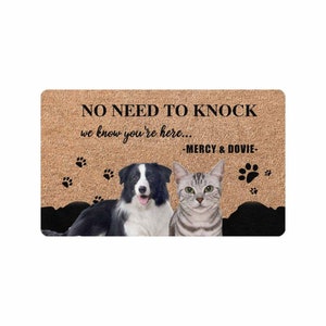 以下が含まれることがあります： 「NO NEED TO KNOCK we know you're here... -MERCY & DOVIE-」と書かれた茶色の玄関マット。黒と白のボーダーコリーと灰色の虎猫がマットの上に座っています。