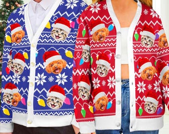 May include: Two button-down cardigans, one blue and one red, featuring a repeating pattern of cats and dogs wearing Santa hats, white snowflakes, and colorful Christmas light bulbs. The cardigans have white trim along the front placket and cuffs.