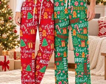 May include: Two pairs of pajama pants with white drawstring waistbands. The left pair is red with a repeating pattern of gingerbread men, Christmas trees, gift boxes, candy canes, and the name Amelia. The right pair is green with the name Robert.