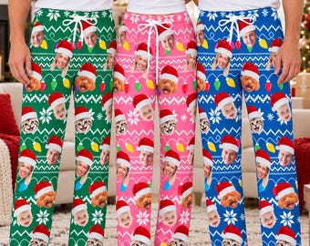 May include: Three pairs of pajama pants in green, pink, and blue, each featuring a repeating pattern of faces wearing Santa hats, colorful Christmas light bulbs, and white snowflake motifs, with a white drawstring at the elastic waistband.