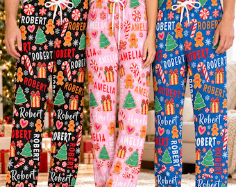 May include: Three pairs of pajama pants featuring a repeating Christmas pattern of gingerbread people, candy canes, gift boxes, and pine trees. The black pants feature the name Robert, the pink pants feature Amelia, and the blue pants feature Robert.