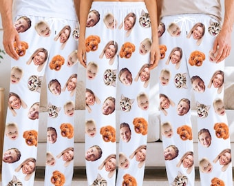May include: White lounge pants featuring an all-over repeating pattern of printed faces of various people, a brown dog, and a tabby cat. The pants have an elastic waistband with a white drawstring tie at the center front.
