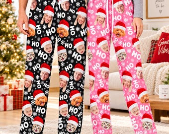 May include: Two pairs of lounge pants, one black and one pink, featuring a repeating pattern of white snowflakes, the text HO, and custom photo faces of people and pets wearing red Santa hats, with white drawstring waistbands on both pairs.