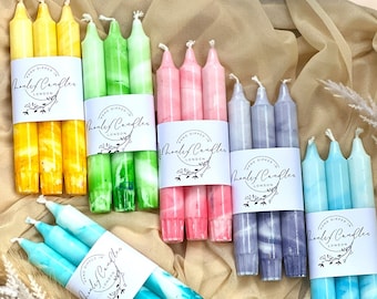 May include: A collection of hand-dipped taper candles in various colors, including yellow, green, pink, purple, and blue. Each set is wrapped with a white label that reads "Hand Dipped in London" and "Henley Candles."