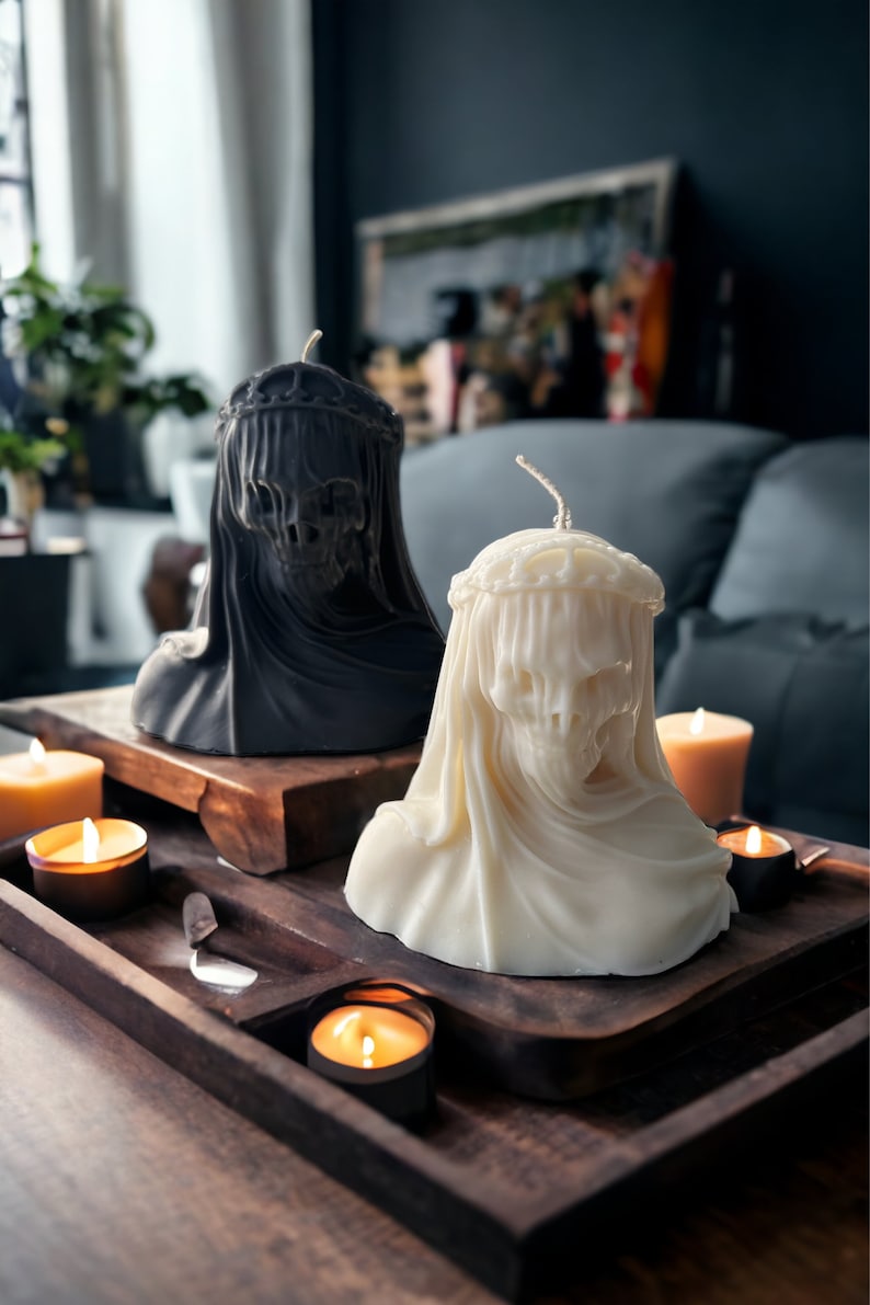 May include: Two decorative candles in the shape of a person's head wearing a veil. The candles are on a wooden tray with other candles.