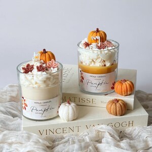 Puede incluir: Dos velas en tarro de cristal con tem&aacute;tica de calabaza especiada. Cada vela tiene una calabaza decorativa en la parte superior, con cera batida blanca y hojas de oto&ntilde;o. Las etiquetas dicen "MONLIK CANDLES LONDON Pumpkin SPICE".