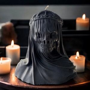 May include: A black candle in the shape of a hooded figure with a crown. The candle is sitting on a wooden tray with other candles.