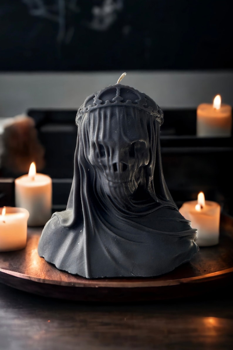 May include: A black candle in the shape of a hooded figure with a crown. The candle is sitting on a wooden tray with other candles.