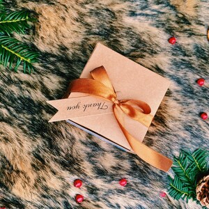 May include: A brown gift box with a gold ribbon and a tag that says "Thank you". The box is on a brown and white faux fur background.