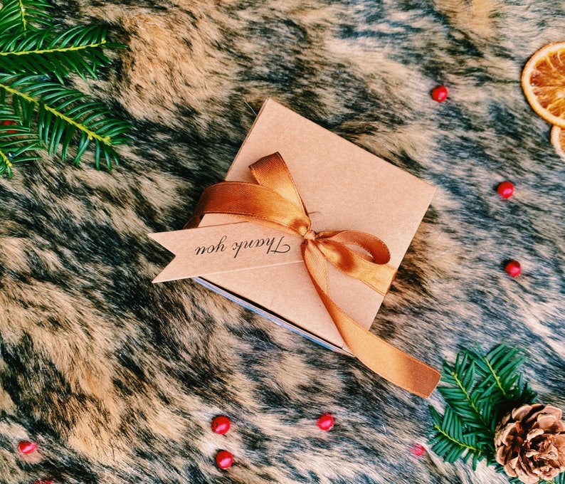 May include: A brown gift box with a gold ribbon and a tag that says "Thank you". The box is on a brown and white faux fur background.