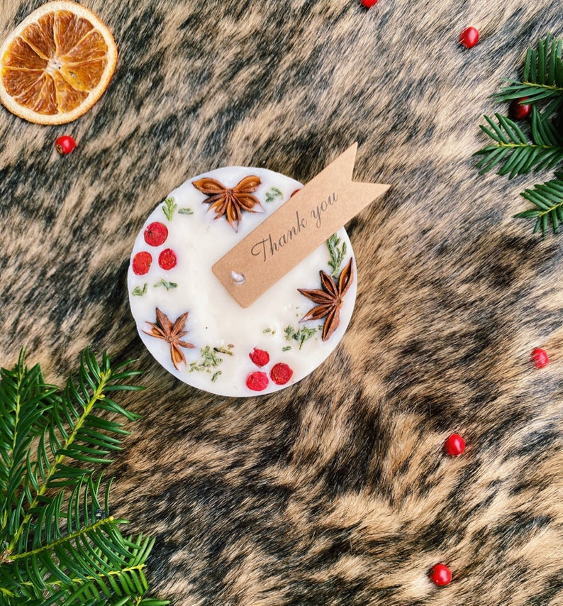 May include: A white candle with a brown tag that says "Thank you". The candle is decorated with dried berries, star anise, and greenery.
