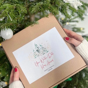 May include: A brown box with a white label that says "Your Winter Date Has Arrived" and "MONLIX CANDLES LONDON". The label also features a watercolor illustration of a forest scene with green trees and gold glitter.