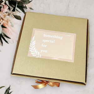 May include: A brown cardboard box with a gold ribbon tied around it. The box has a sticker on it that says "Something special for you" and "Morris Candles London".