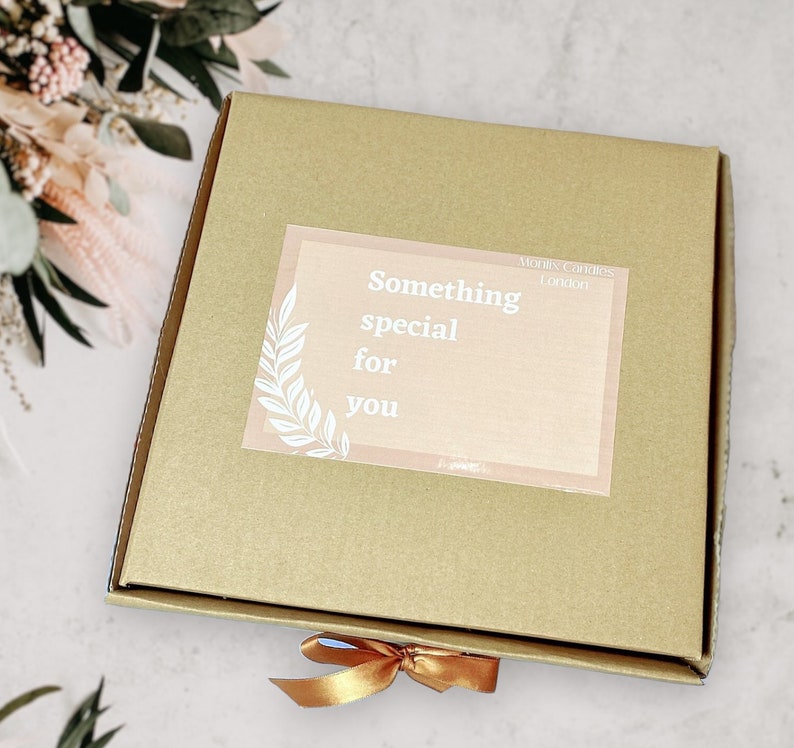 May include: A brown cardboard box with a gold ribbon tied around it. The box has a sticker on it that says "Something special for you" and "Morris Candles London".