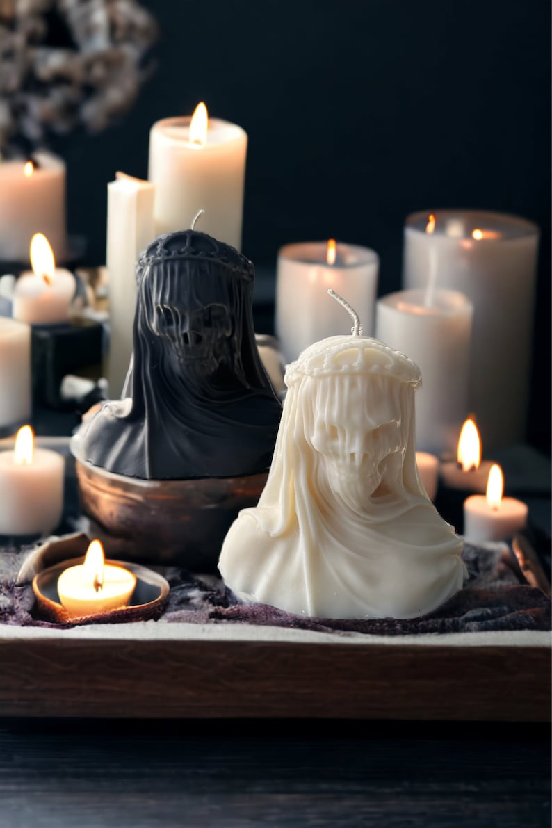 May include: Two white and black skull-shaped candles with a crown on top, surrounded by other candles on a wooden tray.
