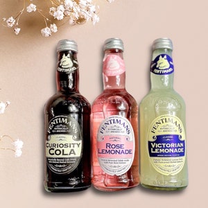 May include: Three glass bottles of Fentimans Botanically Brewed beverages. From left to right: Curiosity Cola, Rose Lemonade, and Victorian Lemonade. Each bottle has a unique label design with a vintage aesthetic.