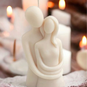 May include: A white candle sculpture of a couple embracing. The candle is made of a smooth, white wax and has a simple, elegant design.