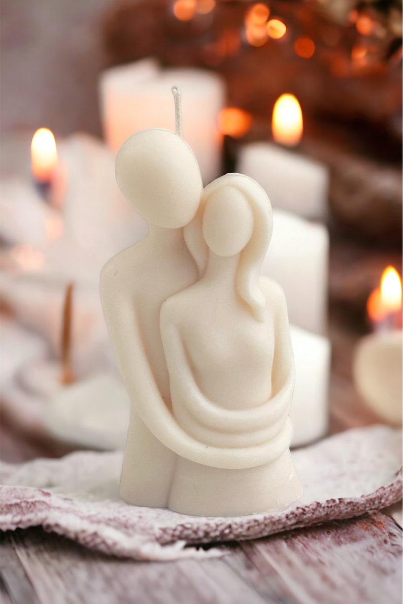 May include: A white candle sculpture of a couple embracing. The candle is made of a smooth, white wax and has a simple, elegant design.