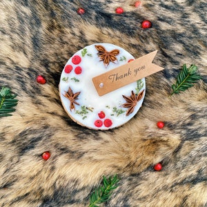 May include: A white candle with dried flowers and star anise on a brown faux fur background. The candle has a brown wooden base and a small brown tag with the text "Thank you" attached.